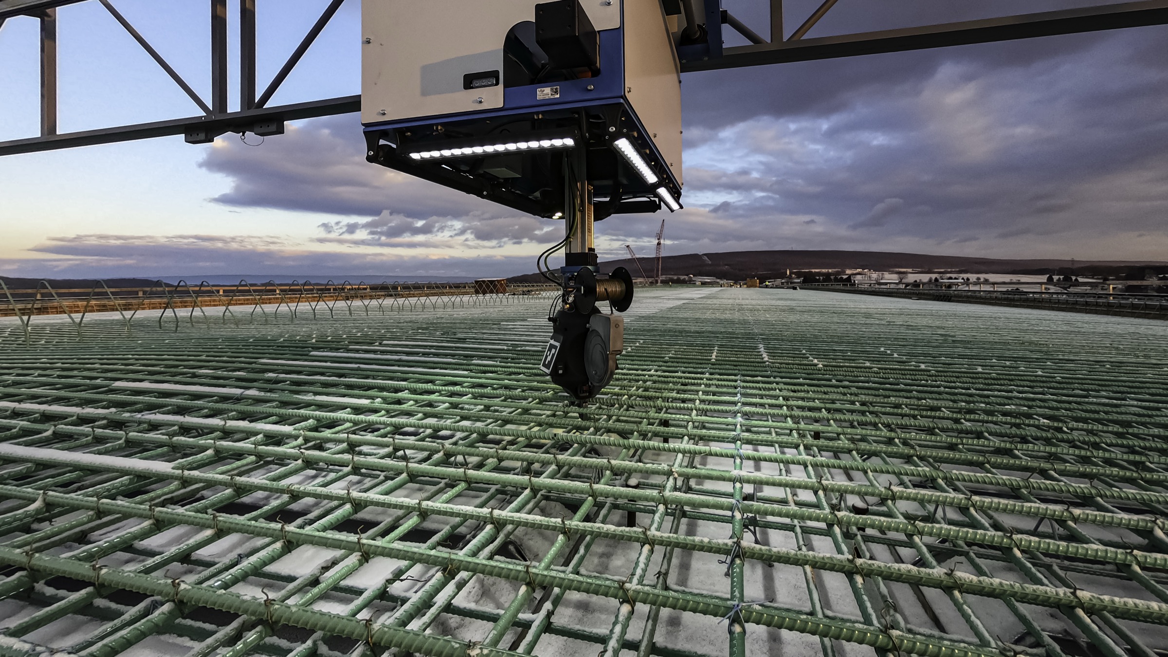 TyBot, a gantry robot, tying rebar intersections on a bridge deck at dusk